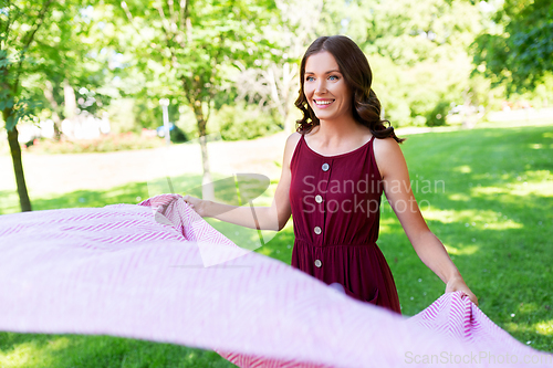 Image of happy woman spreading picnic blanket at park