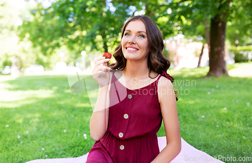 Image of happy woman eating strawberry on picnic at park