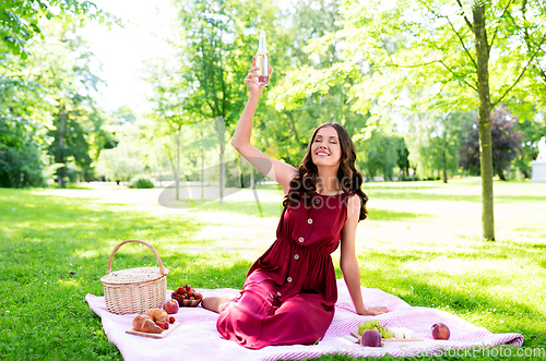 Image of happy woman with picnic basket and drink at park