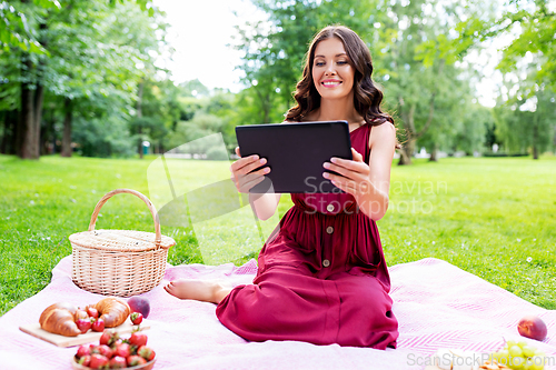 Image of happy woman with tablet computer on picnic at park