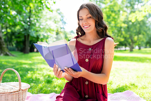 Image of happy woman reading book at picnic in summer park