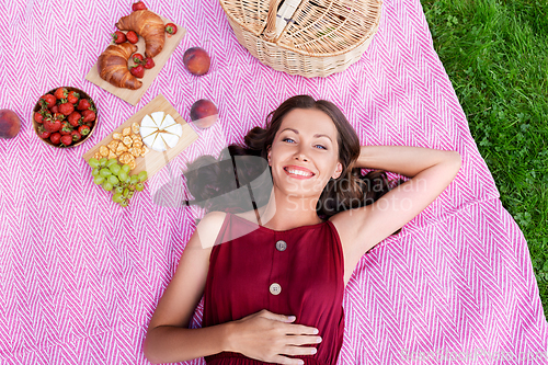 Image of happy woman lying on picnic blanket at summer park