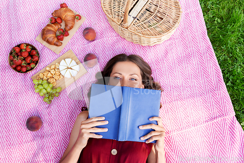 Image of happy woman reading book at picnic in summer park