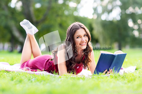 Image of happy smiling woman reading book at summer park