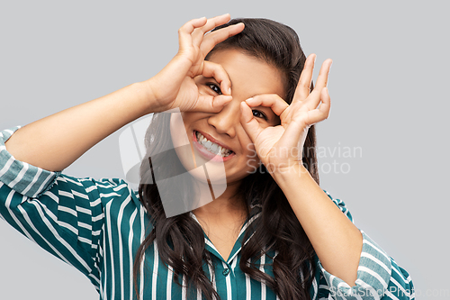 Image of smiling asian woman looking through finger glasses