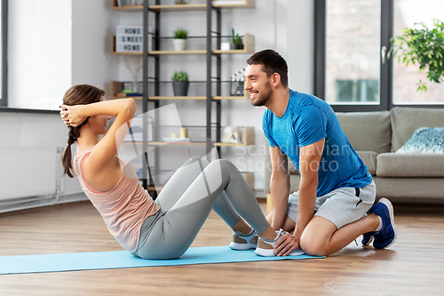 Image of woman with personal trainer doing sit ups at home