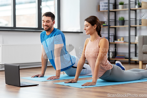 Image of happy couple with laptop exercising at home