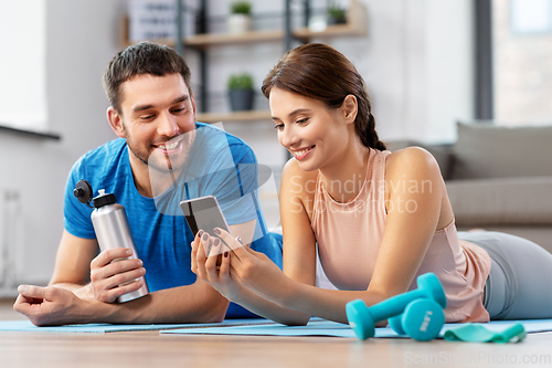 Image of happy couple with smartphone after sports at home