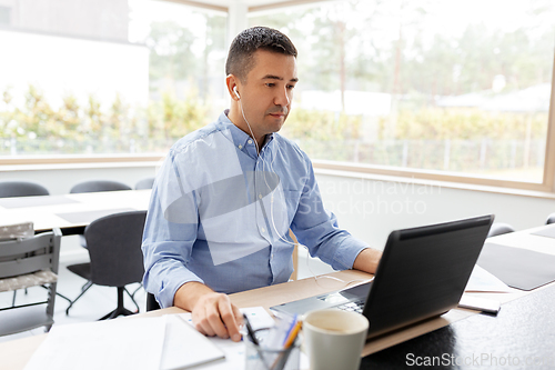 Image of man in earphones with laptop working at home