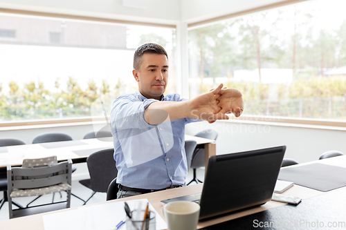 Image of tired man with laptop stretching at home office