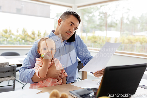 Image of father with baby calling on phone at home office