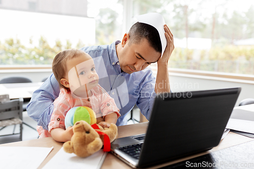 Image of father with baby working on laptop at home office