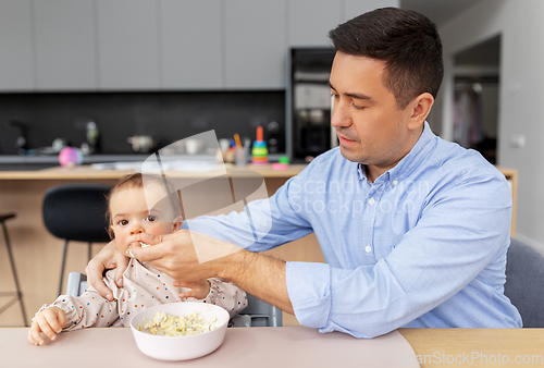 Image of middle-aged father feeding baby daughter at home