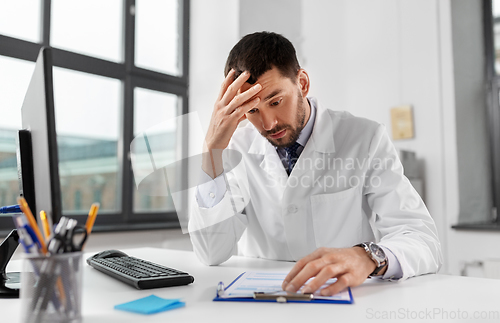 Image of stressed male doctor with clipboard at hospital