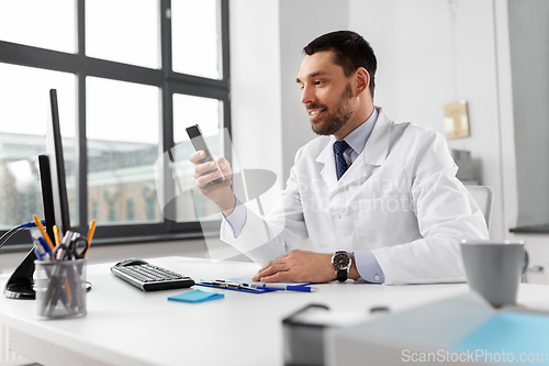 Image of smiling male doctor with smartphone at hospital