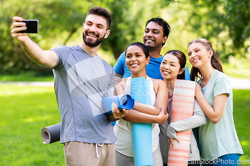 Image of happy people with yoga mats taking selfie at park