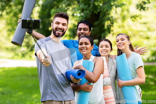 Image of happy people with yoga mats taking selfie at park