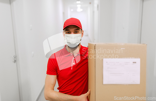 Image of delivery man in mask with parcel box in corridor