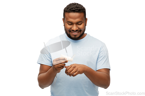 Image of happy african man applying moisturizer to his hand