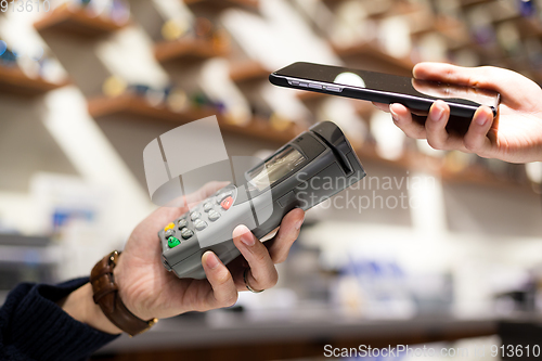 Image of Woman paying with NFC technology on mobile phone in shop