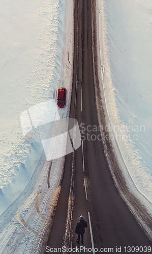 Image of Surreal image with an unusual perspective with a woman on a winter road and car