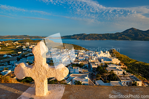 Image of Christian cross and Plaka village on Milos island over red geranium flowers on sunset in Greece