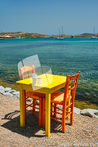 Image of Cafe tableon beach in Adamantas town on Milos island with Aegean sea with boats in background