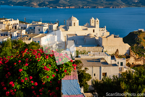 Image of Picturesque scenic view of Greek town Plaka on Milos island over red geranium flowers