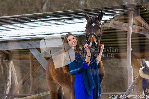 Image of A girl in a blue dress hugs a horse against the backdrop of a snow-covered canopy in the forest