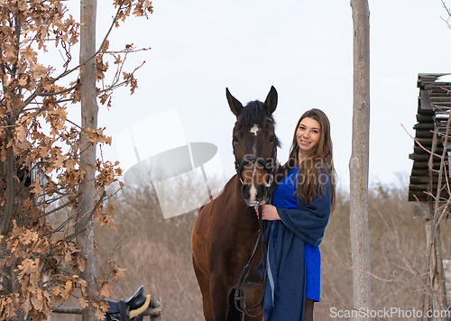 Image of A girl in a blue dress and a horse on the background of a winter forest