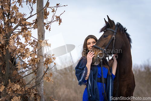 Image of The girl peeks out from behind the muzzle of a horse, in the background an autumn forest