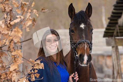 Image of Close-up portrait of a horse and a beautiful girl of Slavic appearance, against the backdrop of a winter forest and an old farm