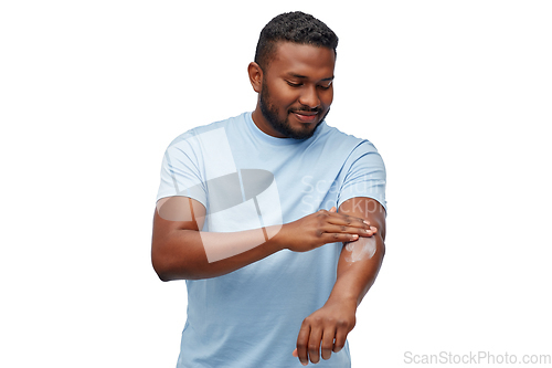 Image of happy african man applying moisturizer to his hand