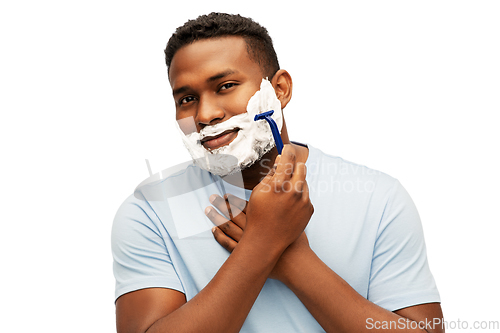 Image of smiling african man shaving beard with razor blade
