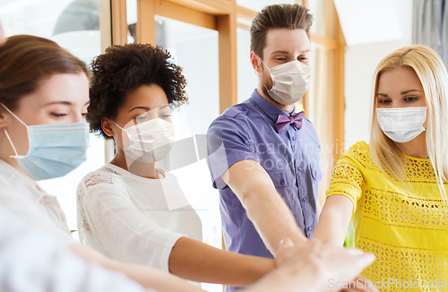 Image of people in masks stacking hands at office