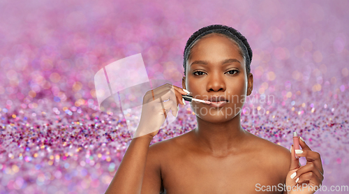 Image of african american woman applying lip gloss