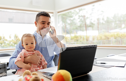 Image of father with baby calling on phone at home office