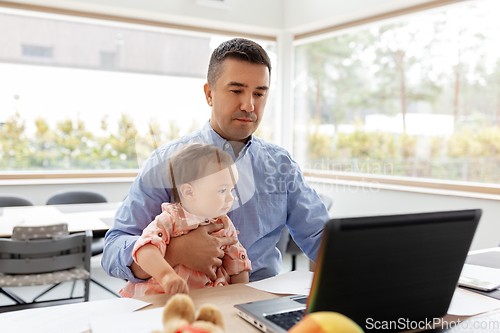 Image of father with baby working on laptop at home office