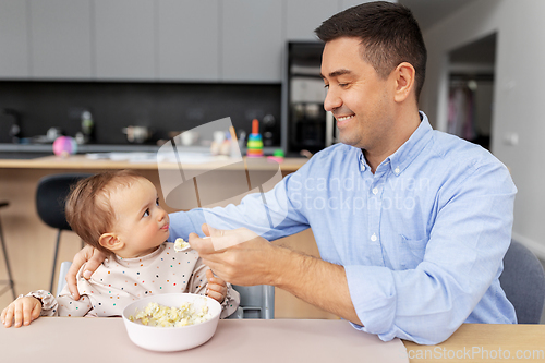 Image of happy father feeding baby in highchair at home