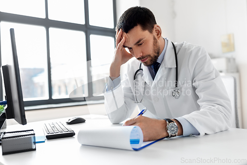 Image of stressed male doctor with clipboard at hospital