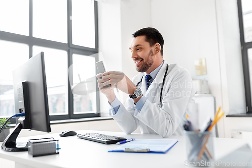 Image of smiling male doctor with smartphone at hospital