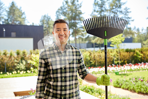 Image of happy middle-aged man with leaf rake at garden