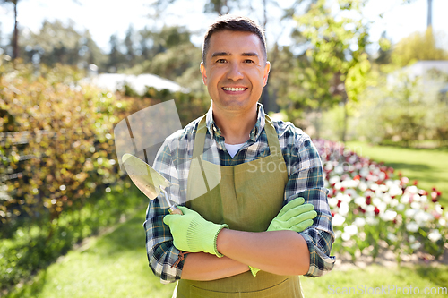 Image of happy man in apron with trowel at summer garden