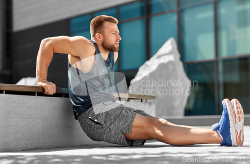 Image of young man doing triceps dip on city street