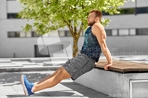 Image of young man doing triceps dip on city street