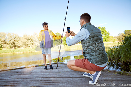 Image of father photographing son with fishing rod on river