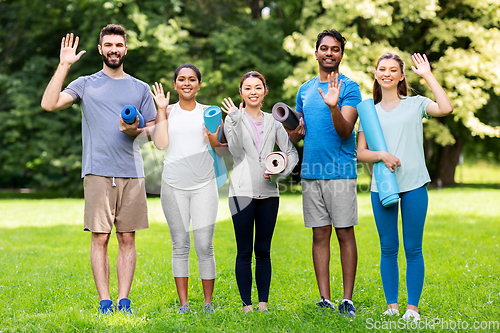 Image of happy people with yoga mats waving hands at park
