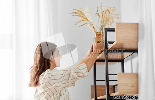 Image of woman decorating home with dried flowers in vase