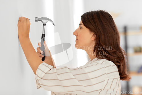 Image of woman hammering nail to wall at home