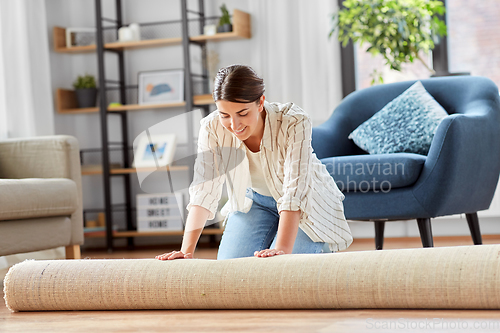 Image of young woman unfolding carpet at home